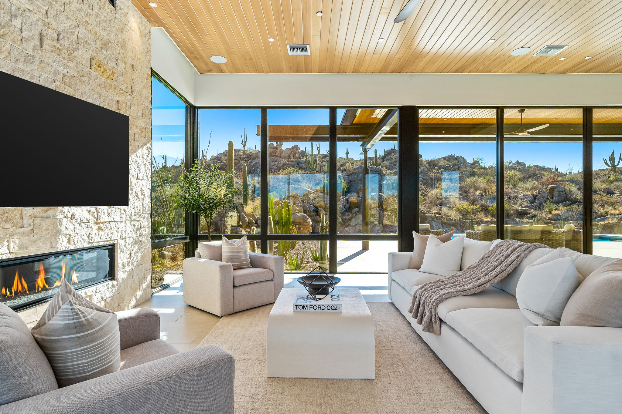Living room with wood ceiling, linear fireplace and glass walls opening to desert views