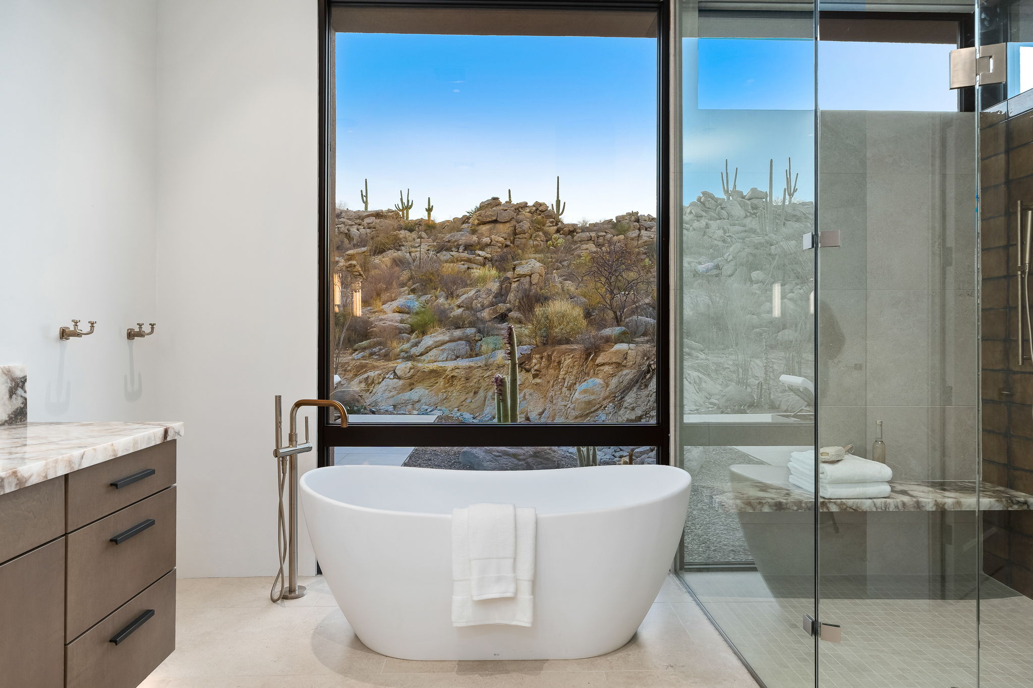 Luxury primary bathroom with freestanding tub and desert boulder views